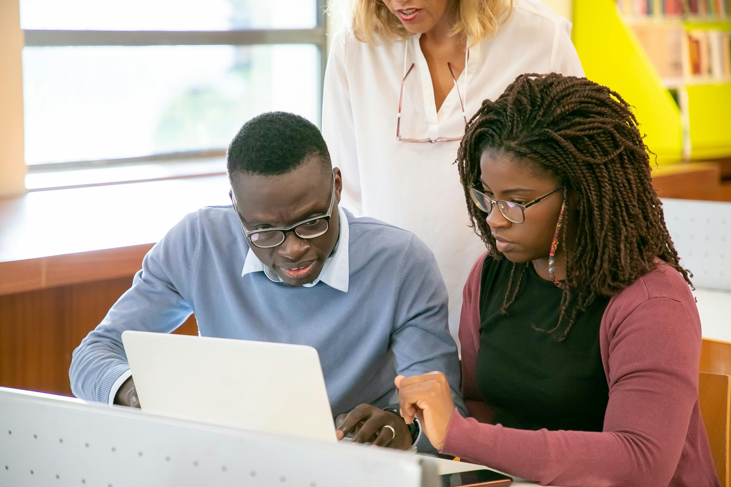A group of diverse students collaborating and studying together on a laptop in a classroom setting.